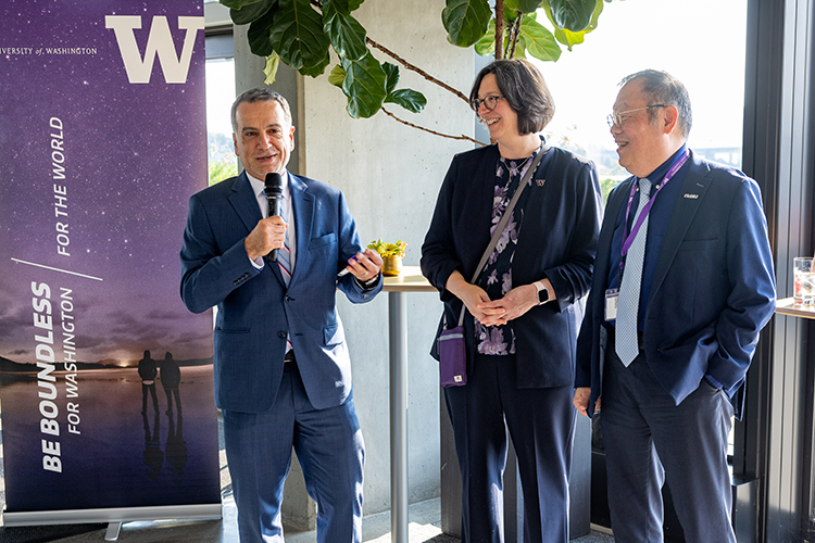 One person talking into a microphone with two other people standing near